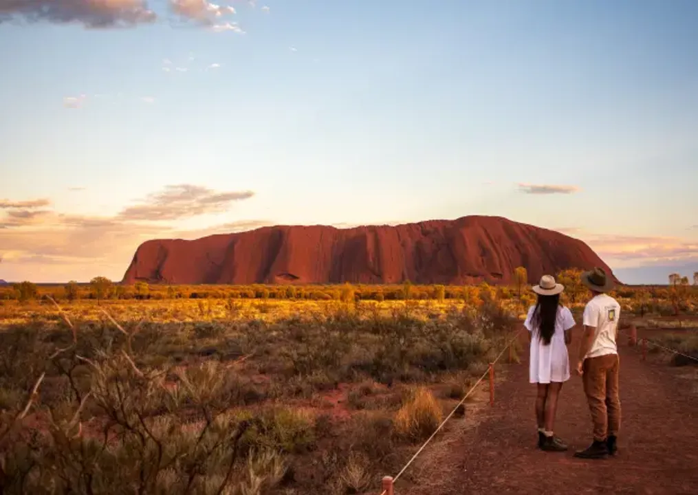 A couple standing to the right with Uluru in the background